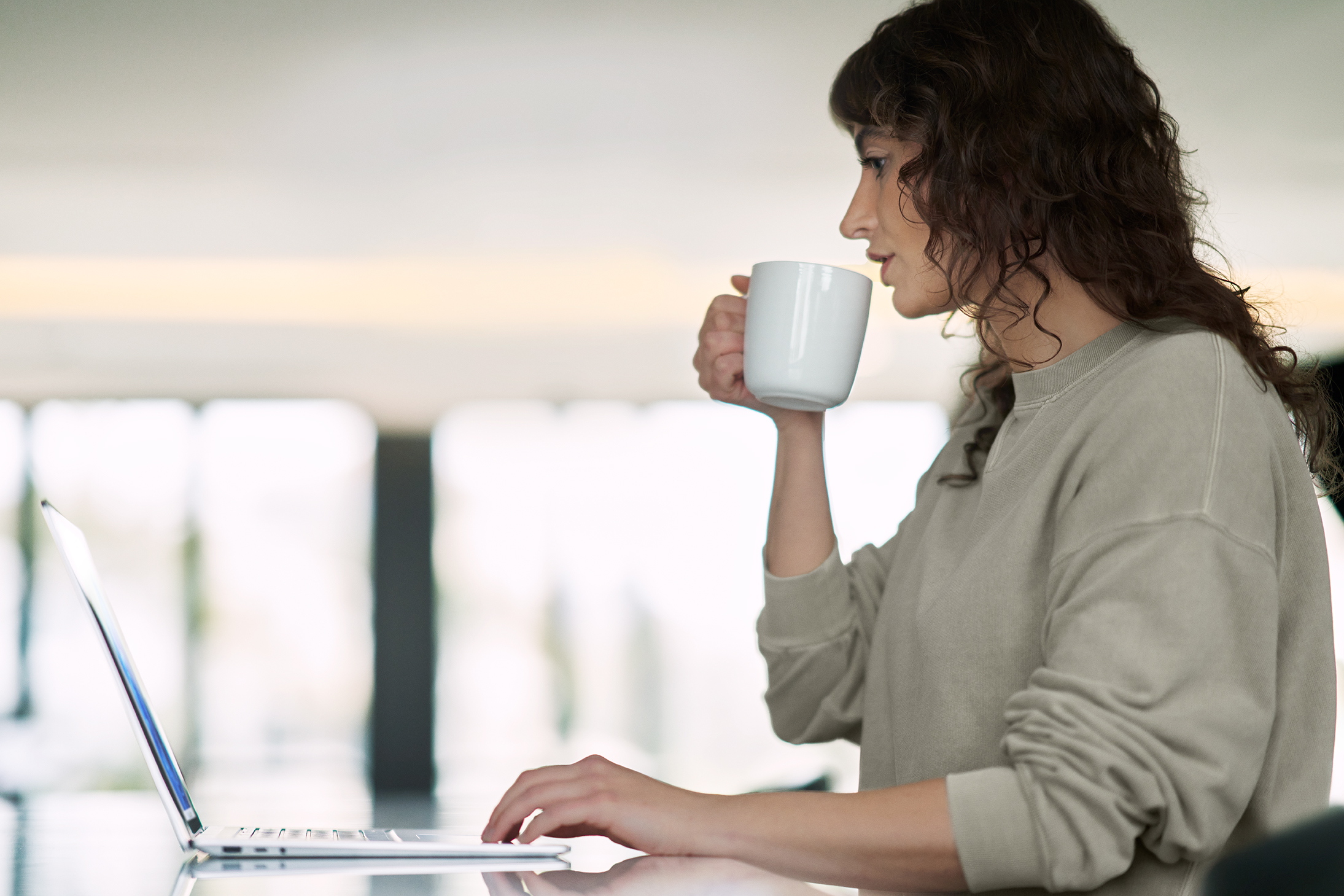 Una mujer trabaja en una laptop mientras toma café