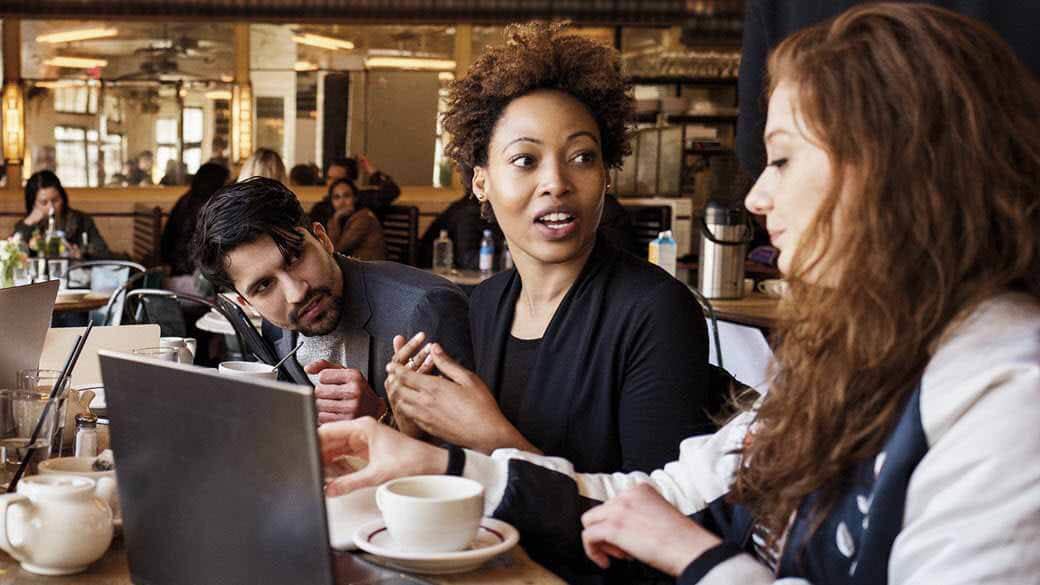 Tres personas en una cafetería frente a una laptop