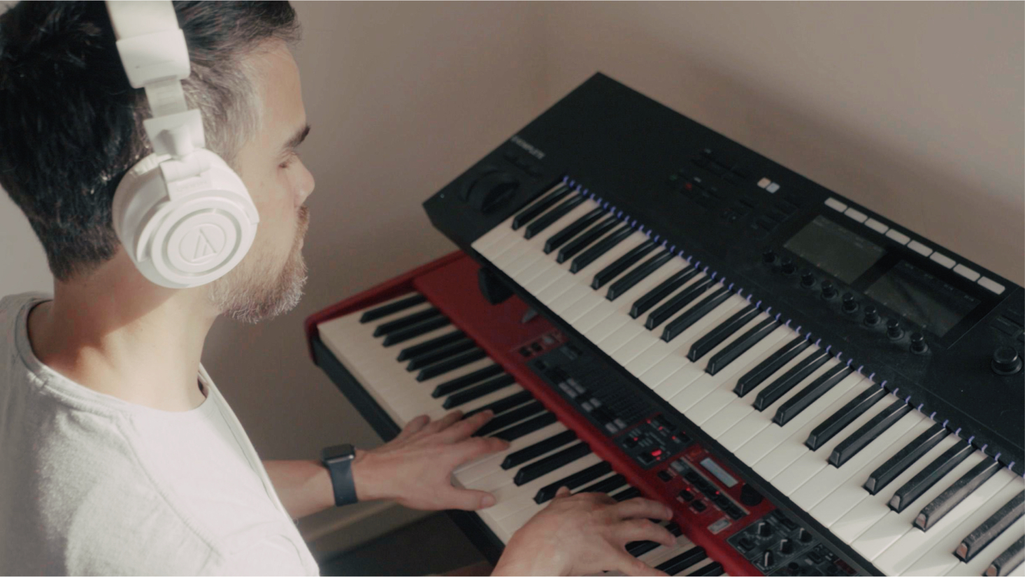 Hombre con auriculares toca un teclado electrónico en una habitación iluminada de manera suave.