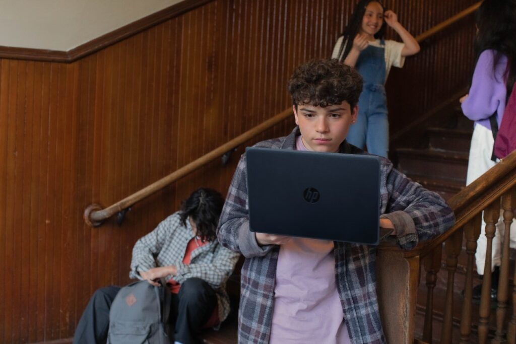 Imagen de un estudiante con una laptop en las escaleras de una escuela