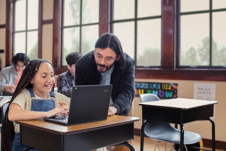 Profesor explica la lección a su alumna en el aula, mientras observan una laptop