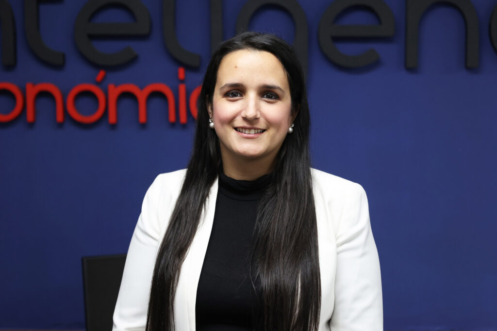 A woman stands in front of a blue wall smiling