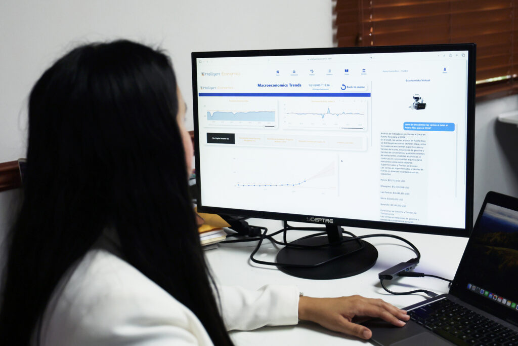 A woman sits at a laptop and an external monitor looking into the screen