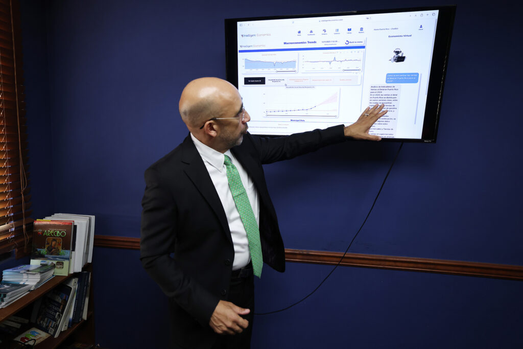 A man stands pointing to a computer monitor mounted on a wall